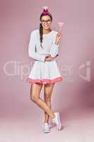 You can entertain yourself. a young woman posing with a party crown and a lollipop against a pink background.