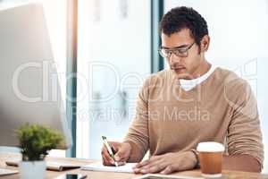 Its easy to design when youve got the right tools. a young designer writing notes while working at his desk in an office.