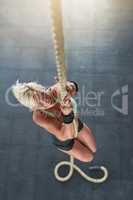 Keep holding on and pushing through. a sporty young woman climbing a rope at the gym.