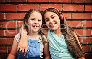 We made a promise to stay friends forever. Portrait of two young girls standing against a brick wall.