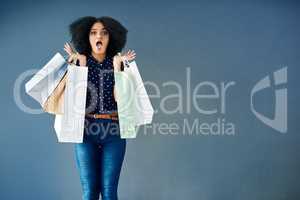 If I couldve bought the whole shop I would have. Studio portrait of a young woman carrying shopping bags and looking surprised against a blue background.