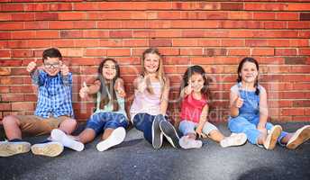 Thumbs up to a blissful childhood. Portrait of a group of young children showing thumbs up against a brick wall.