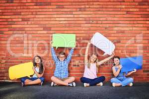 Please listen to what we have to say. Portrait of a group of young children holding speech bubbles against a brick wall.