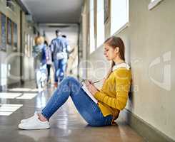 She takes every opportunity to study. Full length shot of an attractive young female student studying in the university corridor.