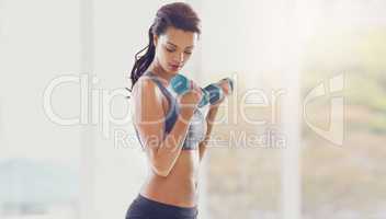 Working on her upper body. an attractive young woman working out with dumbbells in her home.