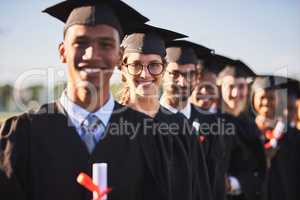 Graduating is both an ending and a beginning. Portrait of a smiling university student on graduation day with classmates in the background.