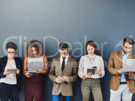 Keeping the anxiety at bay with wireless distractions. Studio shot of a group of businesspeople using wireless technology while waiting in line against a gray background.