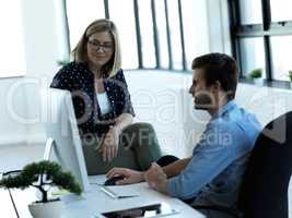 He values her input. two business colleagues chatting at a desk in their office.