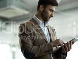 He can almost touch his success. a handsome young businessman working on a tablet in his office.