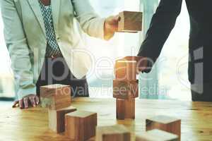 Laying their success on a solid and stable foundation. two unrecognisable businesspeople stacking wooden blocks together in an office.