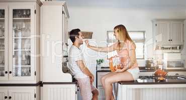 These crips are good but youre even better. a young woman feeding her boyfriend a snack in the kitchen.