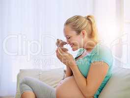 Baby will be as cute and cuddly as tiny teddy. a pregnant woman holding a teddy bear while relaxing at home.