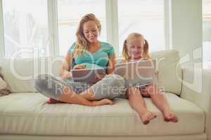 Browsing about all things baby. a pregnant woman and her little daughter using digital tablets at home.