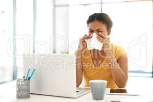 The season of the sniffles. a young businesswoman blowing her nose at her desk in a modern office.