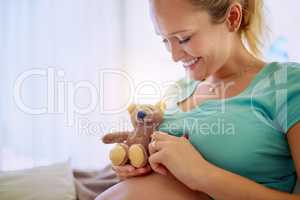 Counting the days till she welcomes her little blessing. a pregnant woman holding a teddy bear while relaxing at home.