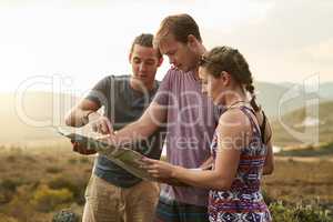 Searching for something undiscovered. three young hikers consulting a map while exploring a new trail.