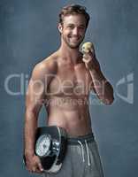 I chose a lifestyle over a diet. Portrait of a healthy young man eating an apple while posing with a scale in studio.