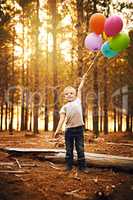 Balloons make me excited. a happy little boy holding a bunch of balloons while standing outside in the woods.