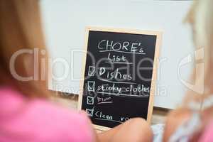 Time for chores. Rearview shot of two little girls looking at a list of chores on a chalkboard at home.