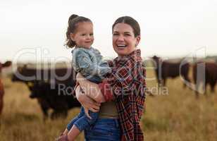 Family, mother and baby on a farm with cows in the background eating grass, sustainability and agriculture. Happy organic dairy farmer mom with her girl and cattle herd outside in sustainable nature