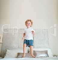 Such joy just jumping on a bed brings him. an adorable little boy jumping on the bed at home.