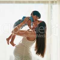 Mommy loves you to the moon and back. a pregnant woman playing with her little boy in her bedroom at home.