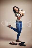 Life is short, buy the shoes. Studio shot of a joyful young woman holding a lot of shoes against a brown background.