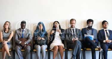 Each candidate has something different to offer. a group of well-dressed businesspeople seated in line while waiting to be interviewed.