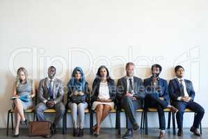 Only the best will make it. a group of well-dressed businesspeople seated in line while waiting to be interviewed.