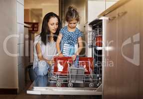 Raising one responsible little girl. a cute little girl and her mother loading the dishwasher together at home.