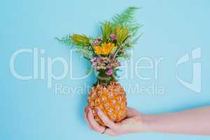 Who says flowers only belong in vases. an unrecognizable woman holding a pineapple stuffed with flowers.