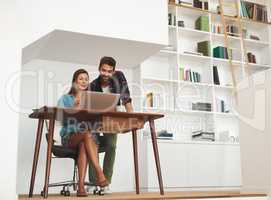 Working on a home-grown business venture. a happy young man checking in on his wife while she works from her desk at home.