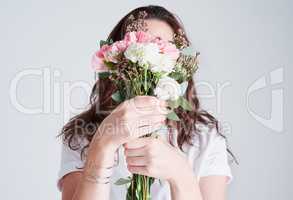 Flowers represents the delicate beauty of a woman. Studio shot of an unrecognizable woman covering her face with flowers against a grey background.