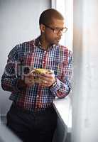 Business man taking a break while looking out of the window. African American male relaxing indoors by viewing outside urban activity. Office worker watching city life below the building.