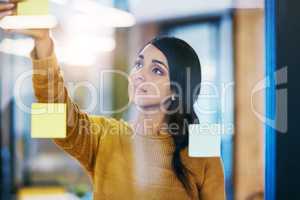 She knows which ideas work the best. a young businesswoman brainstorming with notes on a glass wall in an office.