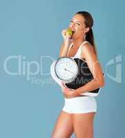 I found the diet that works for me. Studio shot of a fit young woman eating an apple and holding a scale against a blue background.