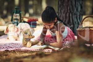 Learning to read is learning to see new worlds. a little girl reading a book with her toys in the woods.