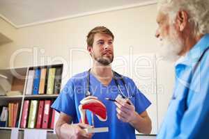 Using visuals to help him understand. a young doctor using a model to explain a diagnosis to his senior patient.