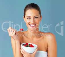 When I eat good I feel good. Studio shot of an attractive young woman eating a bowl of muesli and fruit against a blue background.