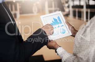 Finding ways to push their profits up. Closeup shot of two unrecognisable businesspeople analysing graphs on a digital tablet in an office.