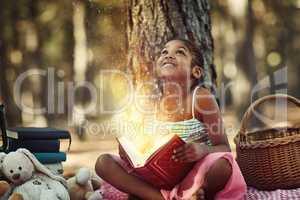 Books open up bright new worlds. a little girl reading a book with glowing pages in the woods.