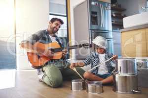 Take it away, son. a happy father accompanying his young son on the guitar while he drums on a set of cooking pots.