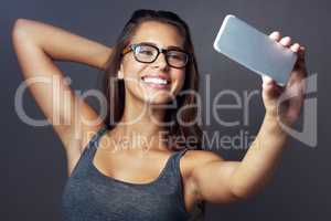 Give a stranger one of your smiles. Studio shot of an attractive young woman taking a selfie against a grey background.