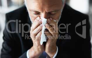 Got to make sure this cold doesnt beat me. a frustrated businessman using a tissue to sneeze in while being seated in the office.