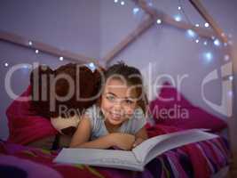 Reading lights up her imagination. Portrait of a little girl reading a book in bed with her teddybear.