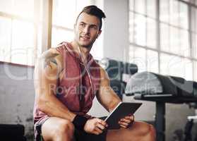 Finding the perfect tune to workout to. a handsome young man using a tablet at the gym.