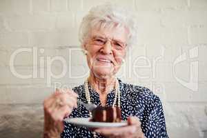 Retirement never tasted this sweet. a senior woman eating a slice of cake inside.