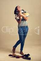 Shoes will always be my first love. Studio shot of a joyful young woman holding a lot of shoes against a brown background.