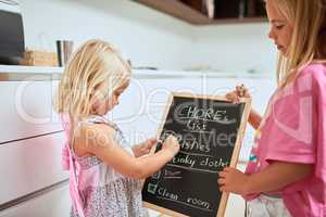 Theyre always willing to help with housework. two little girls writing a list of chores on a chalkboard at home.