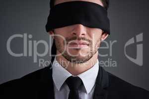 Trust the unseen. Studio shot of a young businessman wearing a blindfold against a gray background.